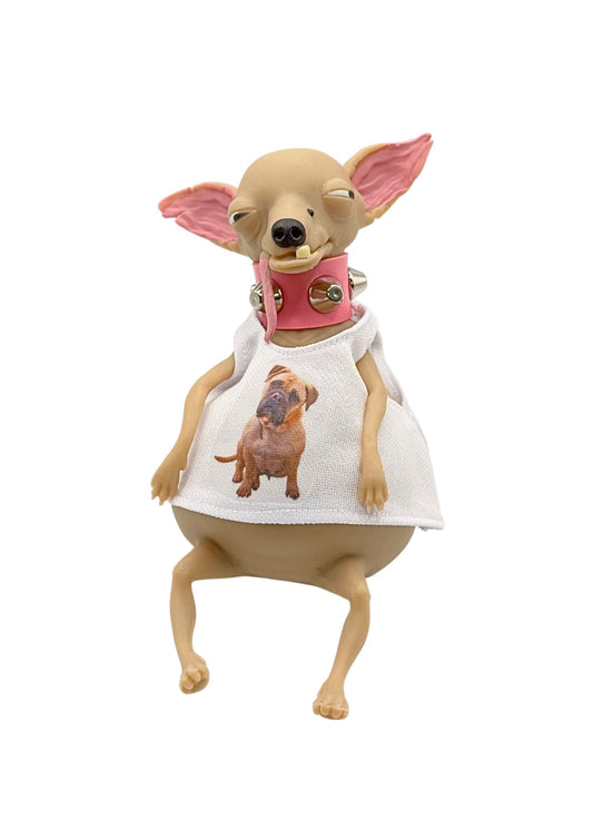 A novelty figurine of a Chihuahua dog wearing a white dress with a printed dog graphic and a pink collar with silver bells, set against a plain white background.
