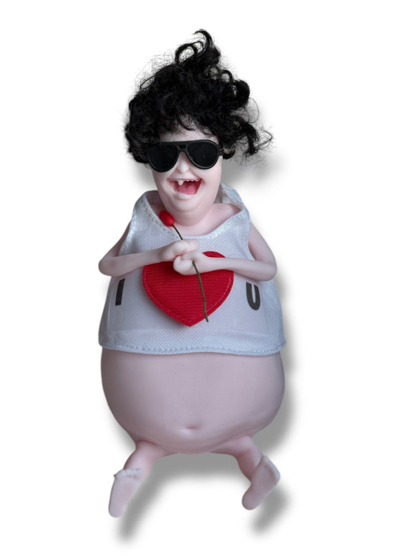 A doll with dark hair, wearing glasses and a white shirt with the text 'I Love U' holding a miniature rose.