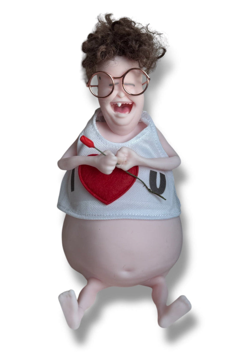 A doll with dark hair, wearing glasses and a white shirt with the text 'I Love U' holding a miniature rose.