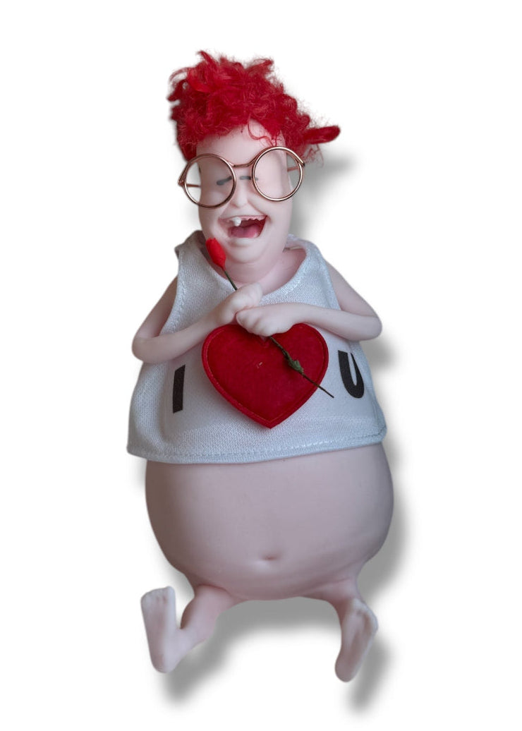 A doll with dark hair, wearing glasses and a white shirt with the text 'I Love U' holding a miniature rose.